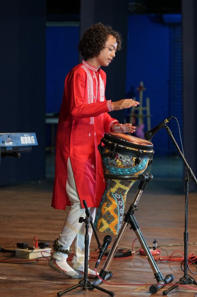 Aurum playing the djembe on stage in a red kurta