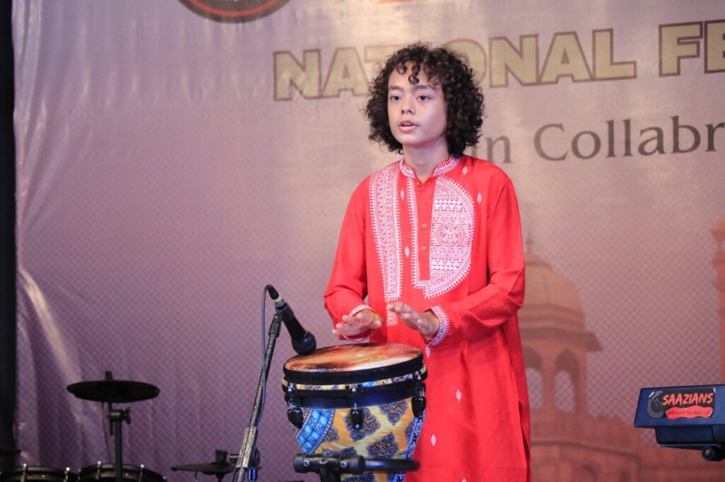 Aurum playing the djembe in front of a festival backdrop